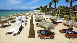 A beach resort with rows of sun loungers and thatched umbrellas, a wooden walkway, and palm trees. - Ilio Mare Resort Hotel by GHH (Thasos)