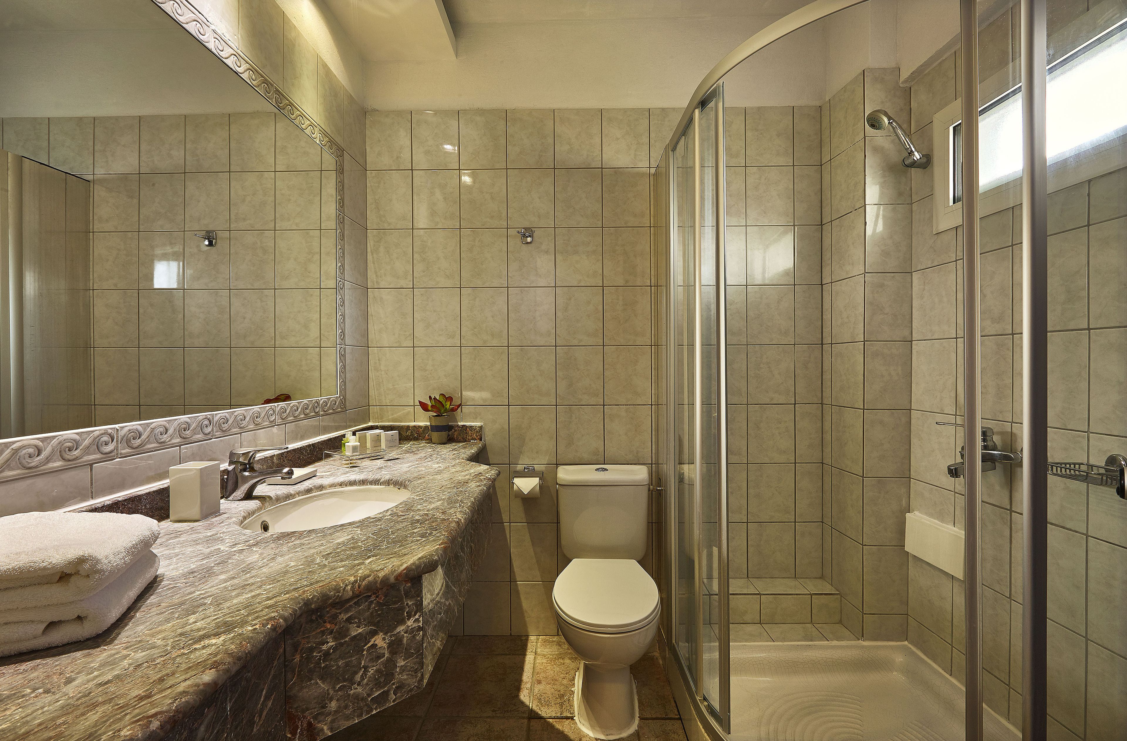 A modern bathroom with a marble sink, a toilet, and a glass-enclosed shower.