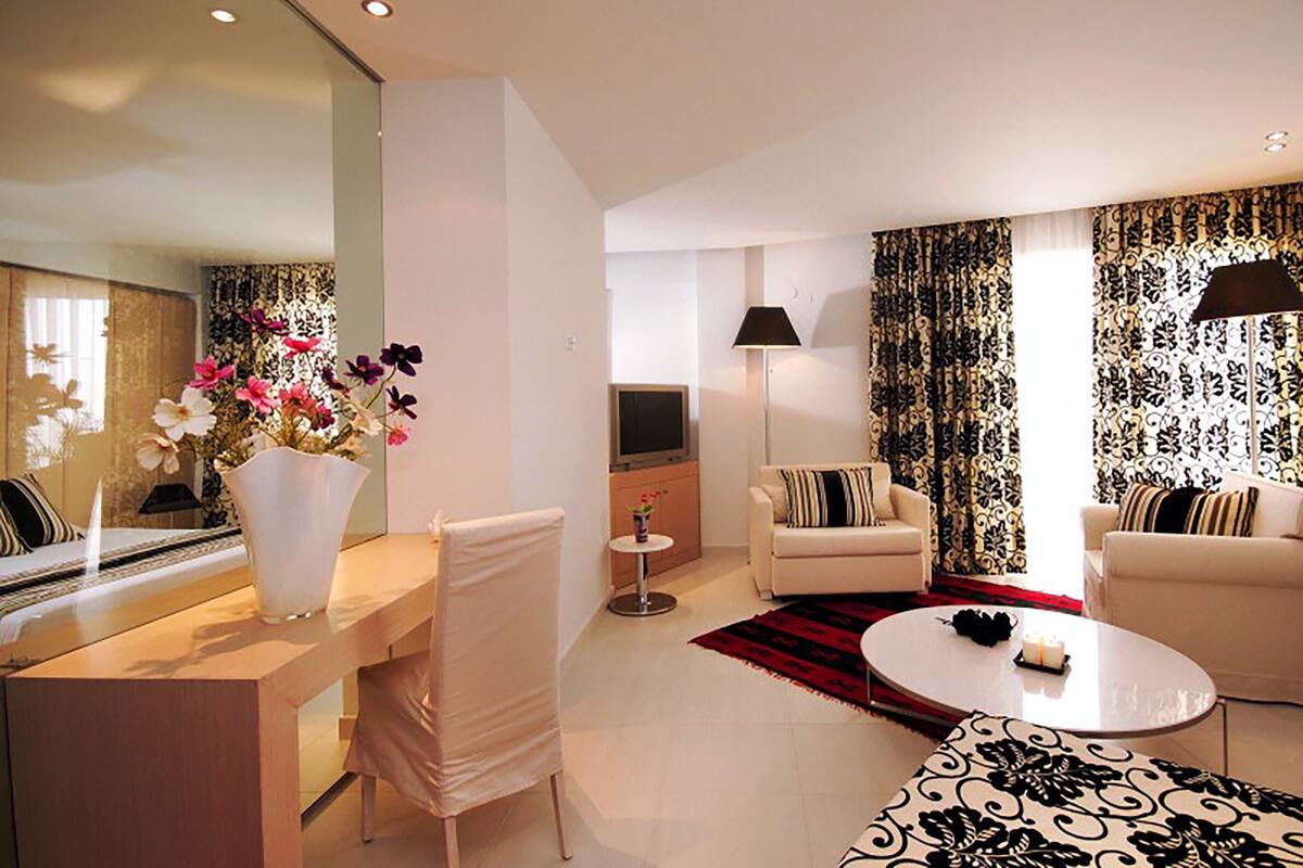 Un salon moderne avec un canapé, des fauteuils, une table basse et un téléviseur. Un vase rempli de fleurs est posé sur une table d’appoint.