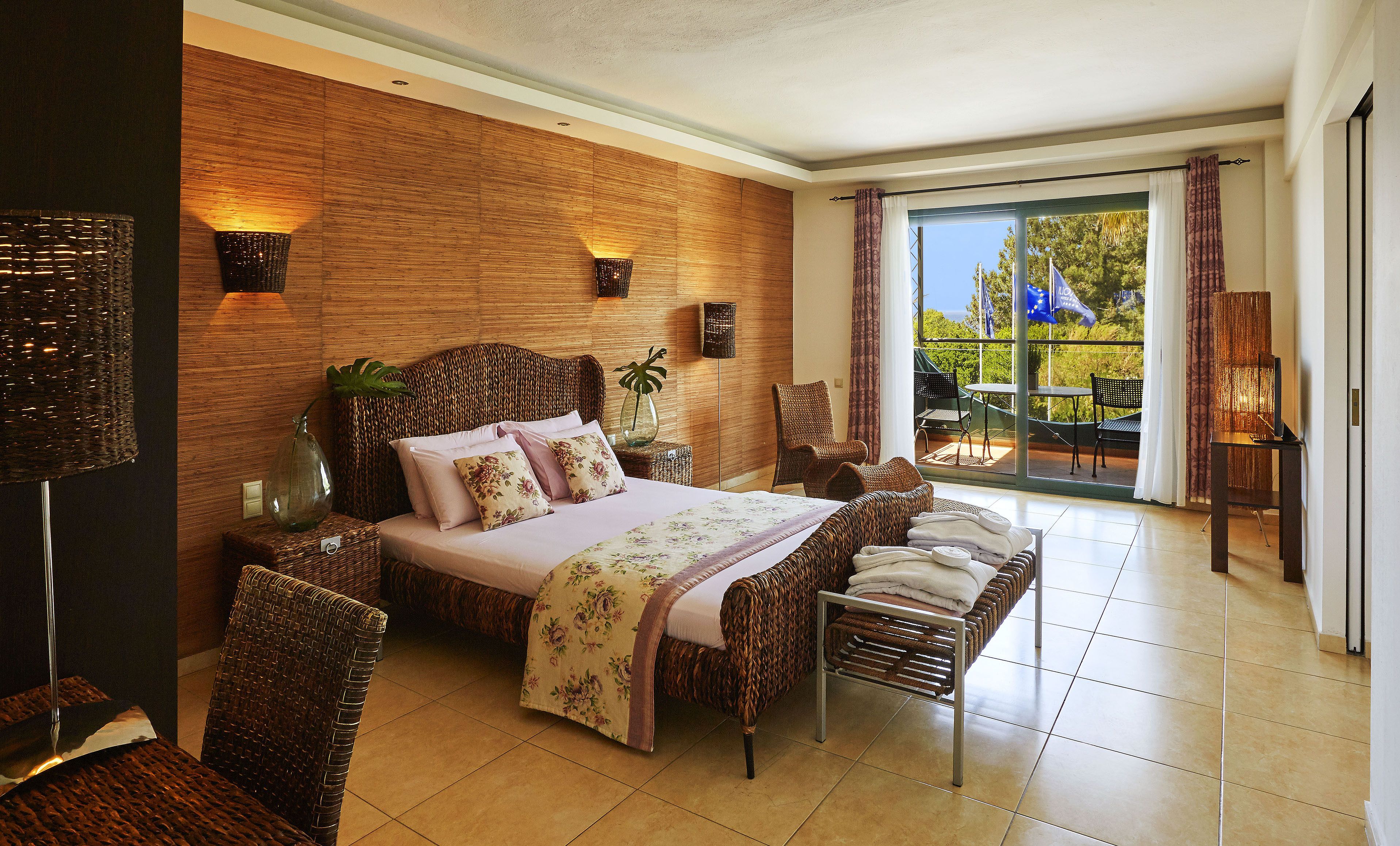 Un dormitorio amplio con una cama grande, muebles de mimbre y vistas al exterior a través de un ventanal corredero.