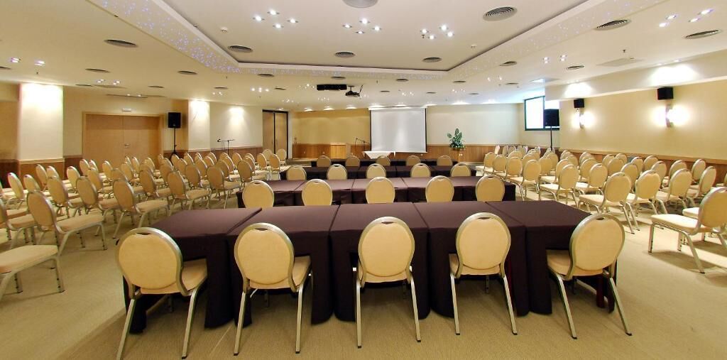 A conference room with multiple tables and chairs, equipped with a projector screen and a speaker.