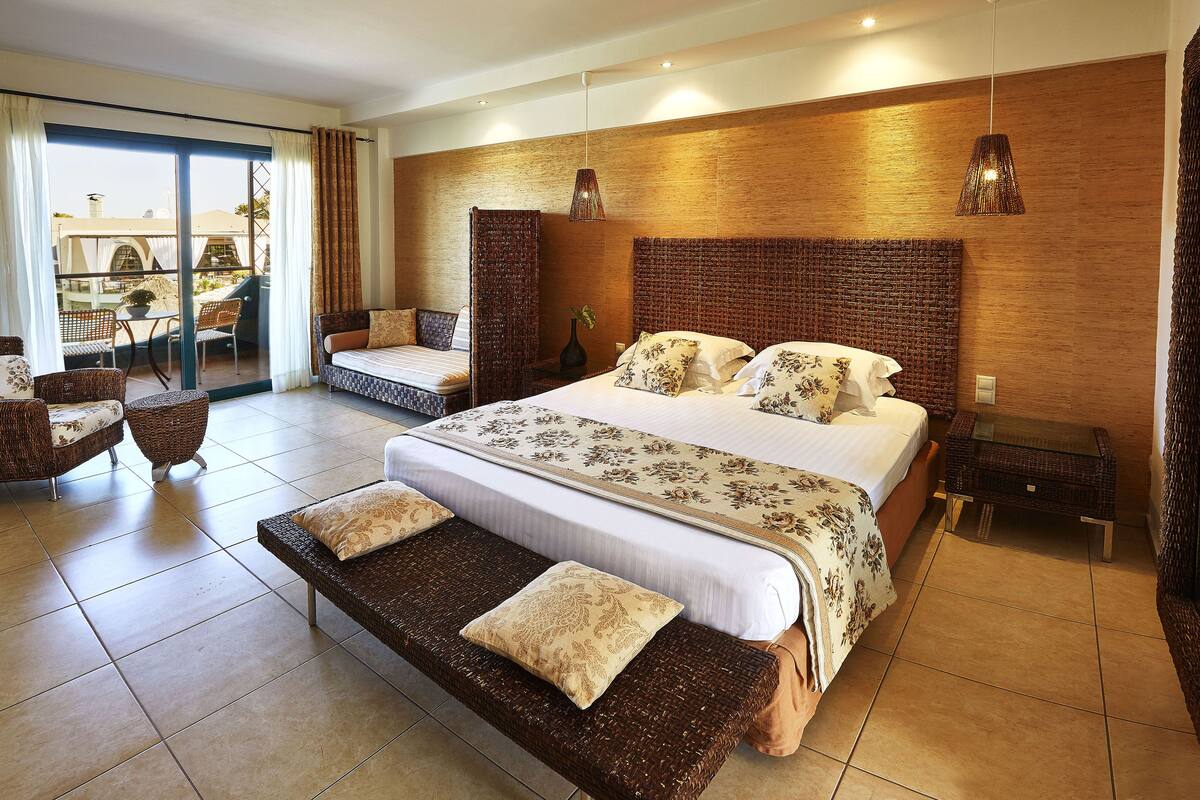 Une chambre spacieuse dotée d’un grand lit, d’un coin salon et d’un balcon aménagé avec du mobilier d’extérieur.