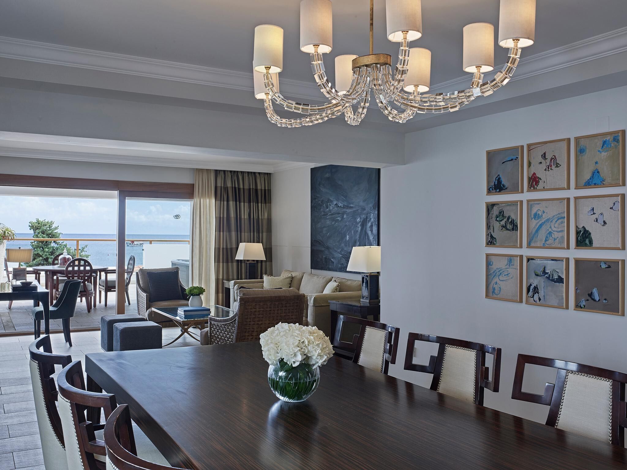 A spacious dining area with a wooden table and chairs, a chandelier, and a large painting on the wall.