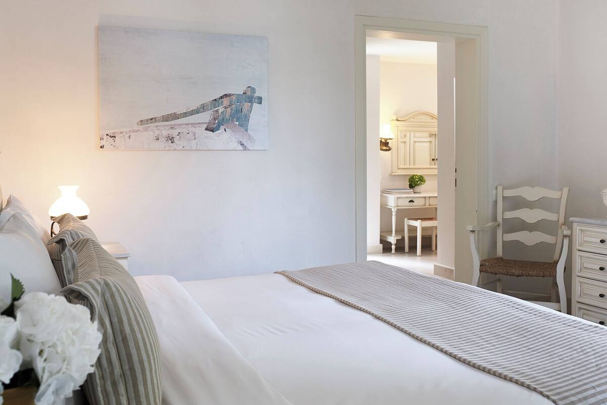 A bedroom with a bed, bedside table, lamp, and a painting on the wall.