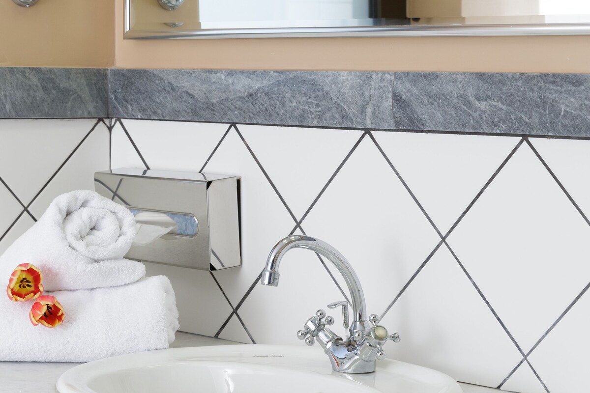 A bathroom with a white sink, a mirror above it, and a towel rack with towels.