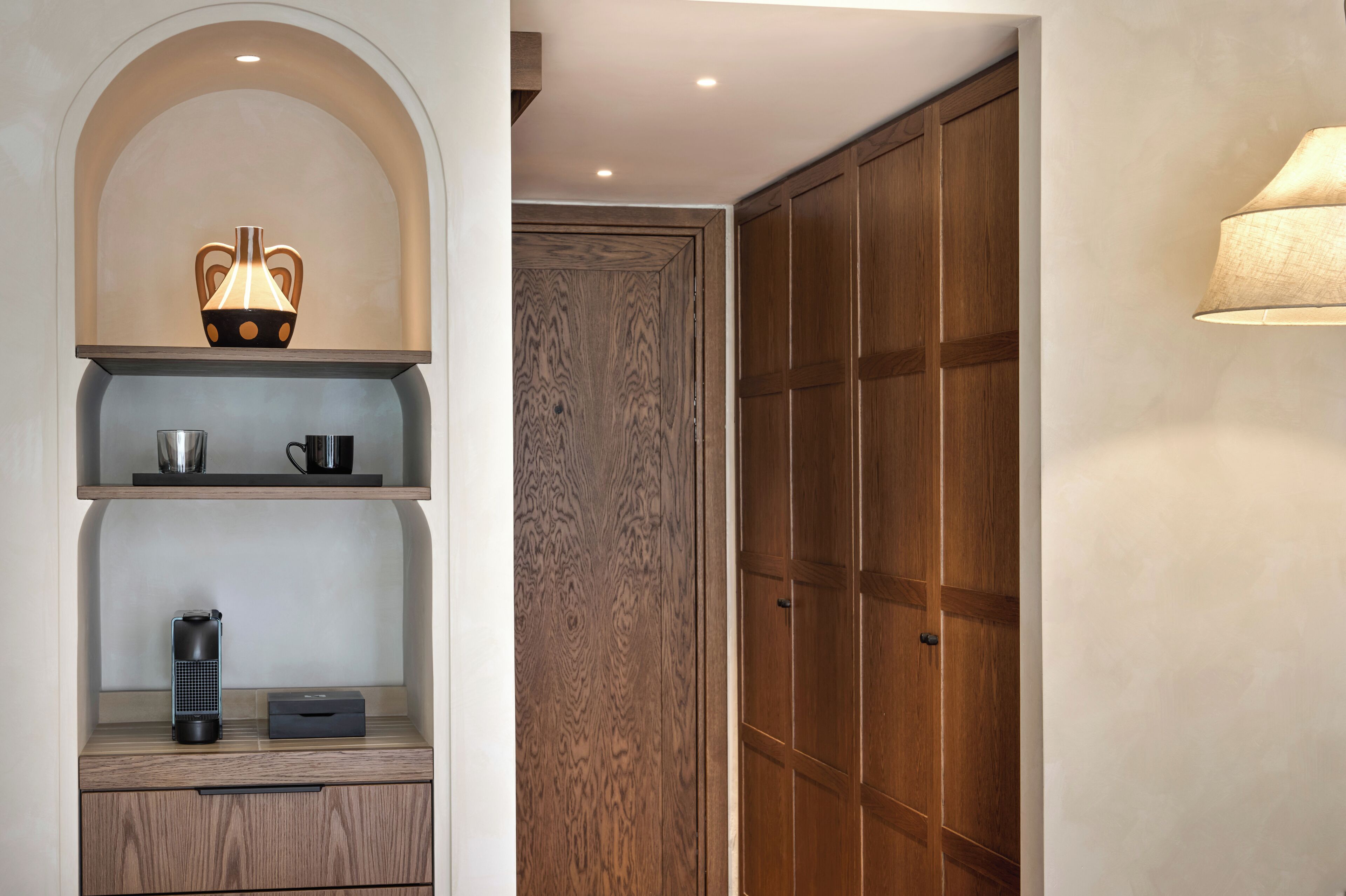 A room with a wooden wardrobe, a shelf with a vase, a kettle, and a coffee maker.