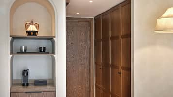 A room with a wooden wardrobe, a shelf with a vase, a kettle, and a coffee maker.