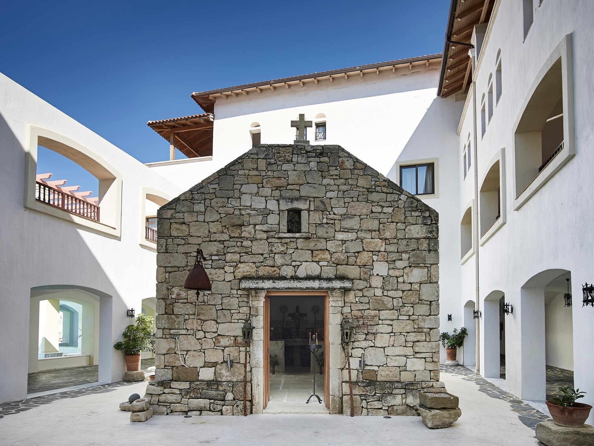 Un edificio de piedra con una cruz en la parte superior, rodeado de edificios blancos con balcones.