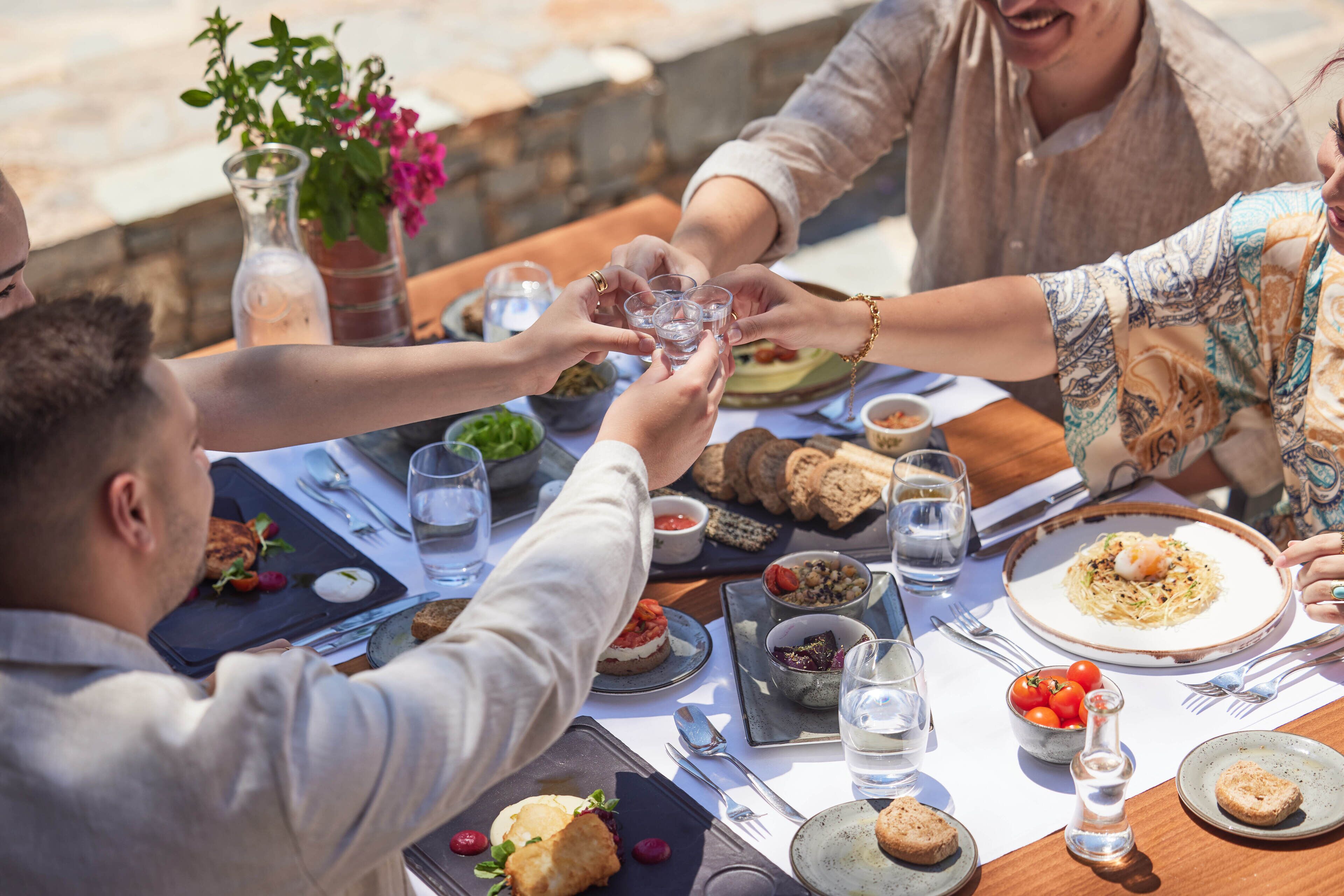 Un groupe de personnes trinquant avec des verres autour d’une table où sont servis différents plats et boissons.