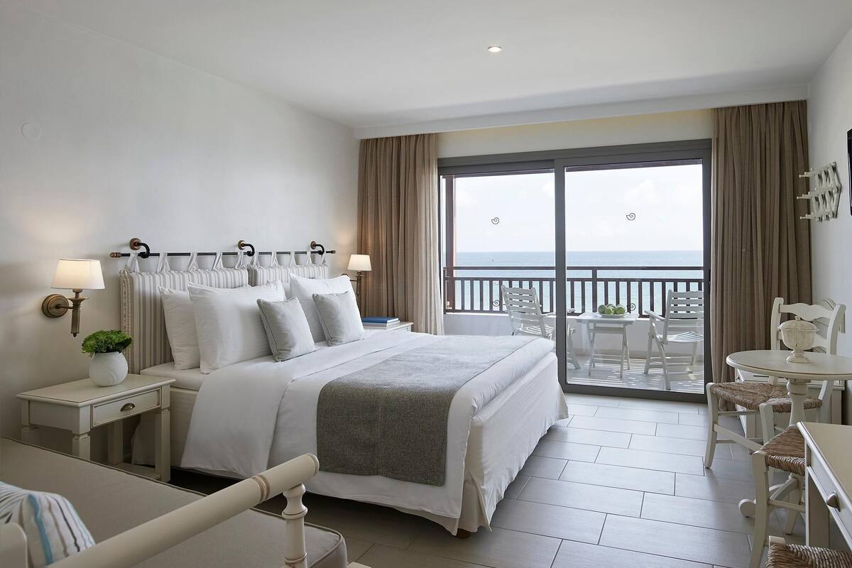 A hotel room with a bed, bedside tables, a desk, and a balcony with chairs and a table.