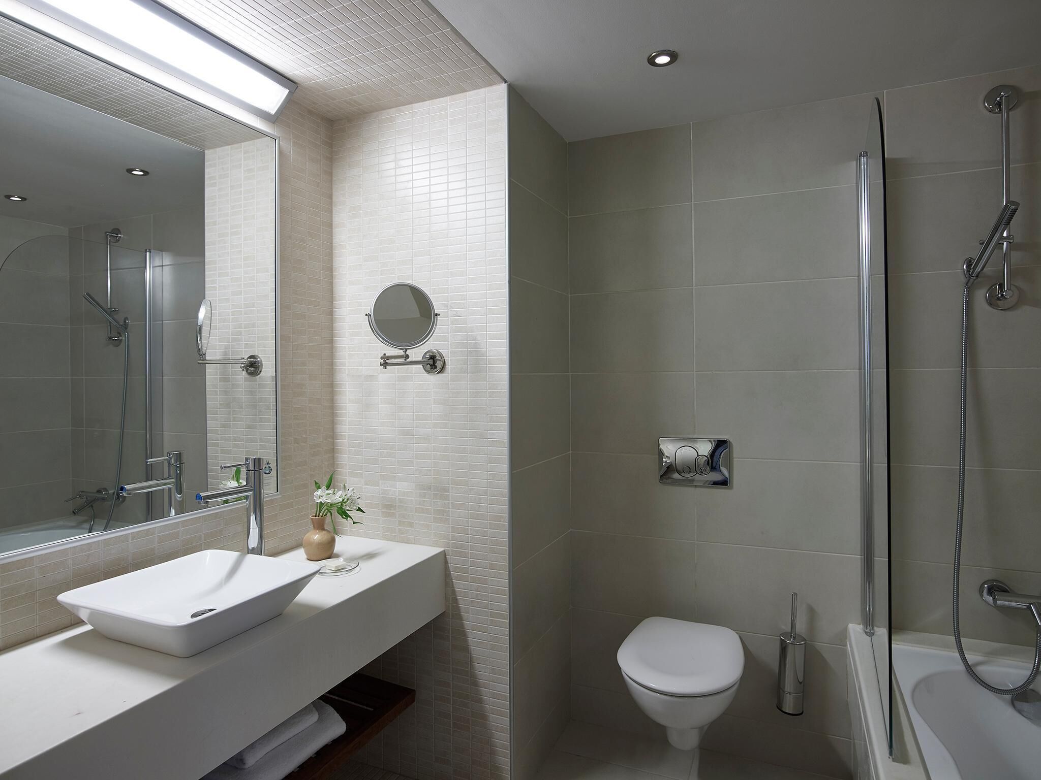 A modern bathroom with a large mirror, a sink, a toilet, and a shower.