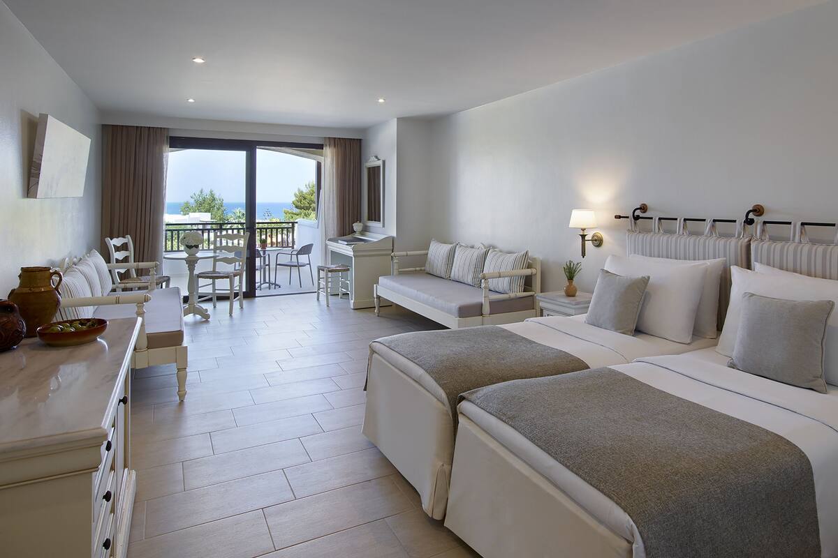 A hotel room with a balcony, a desk, a sofa, and a bed.