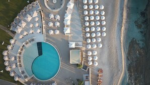 An aerial view of a resort with a large central pool, multiple sun loungers, and umbrellas arranged around the pool area. - Creta Maris Resort - All Inclusive (Hersonissos)
