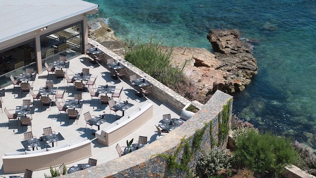 An outdoor terrace with tables and chairs, overlooking a rocky coastline and clear blue waters. - Creta Maris Resort - All Inclusive (Hersonissos)