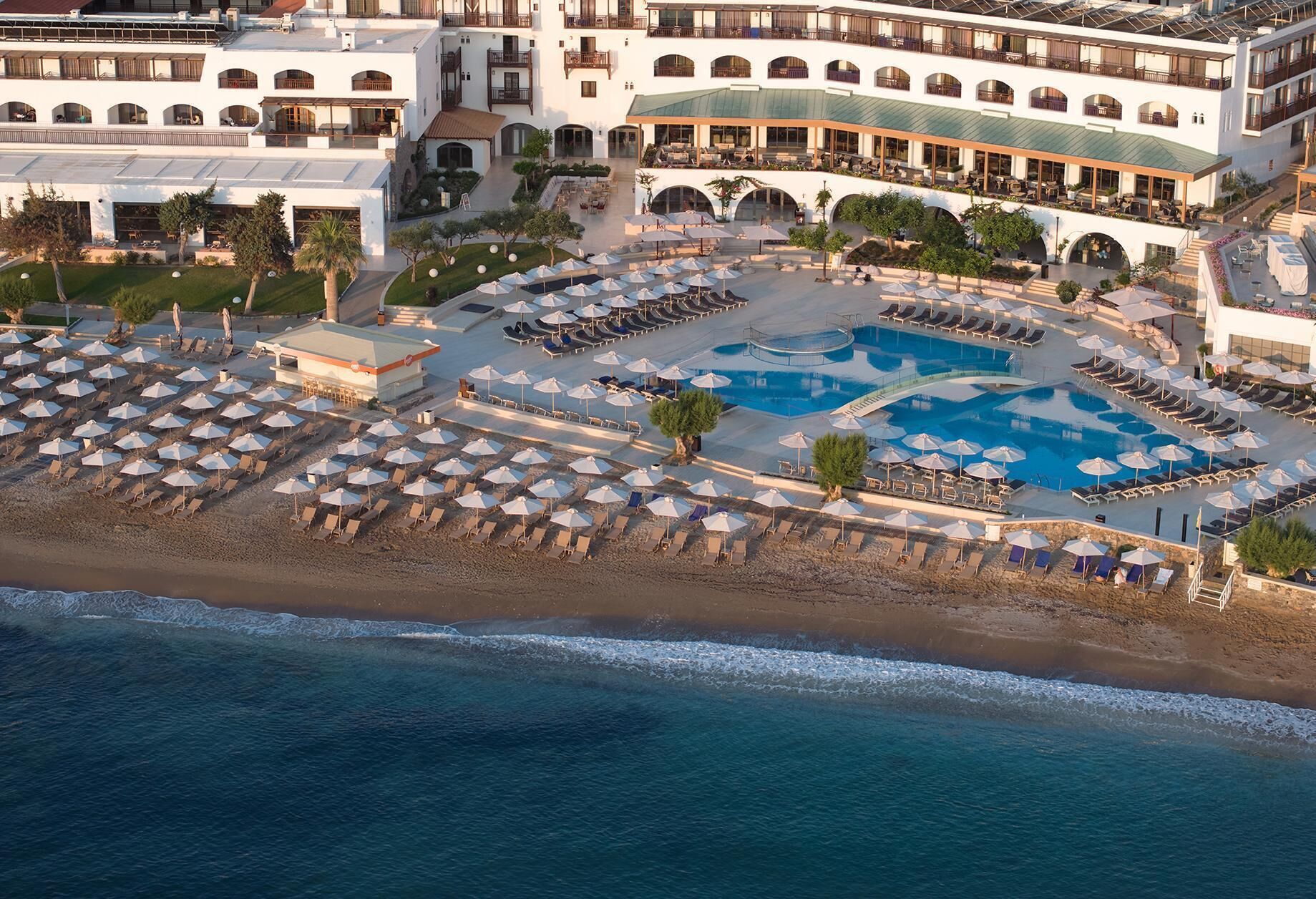 An aerial view of a resort with a large pool, multiple sun loungers, and a beach area.