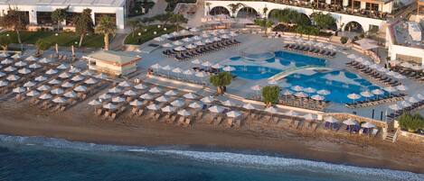 An aerial view of a resort with a large pool, multiple sun loungers, and a beach area.