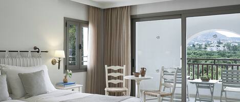 Habitación de hotel con cama, mesita de noche, lámpara y vistas a un balcón con mobiliario exterior.