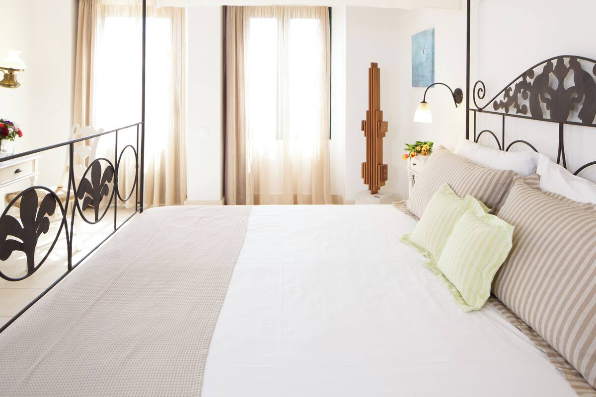 A bedroom with a bed, curtains, a nightstand, a lamp, and a painting on the wall.