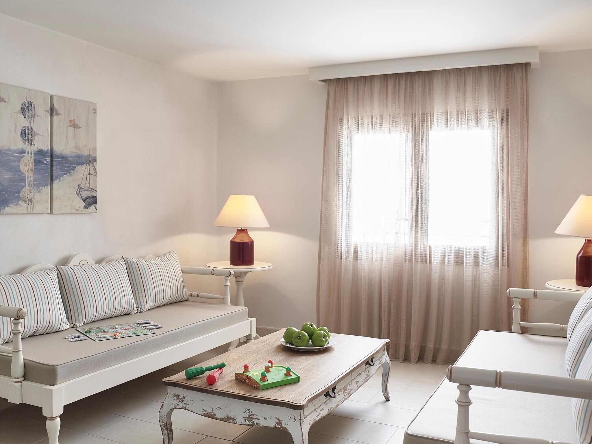 A living room with a sofa, two side tables with lamps, a coffee table with decorative items, and a large window with sheer curtains.