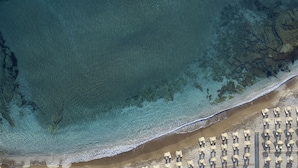 An aerial view of a beach with rows of umbrellas and lounge chairs, a clear blue sea, and a sandy shore. - Creta Maris Resort - All Inclusive (Hersonissos)
