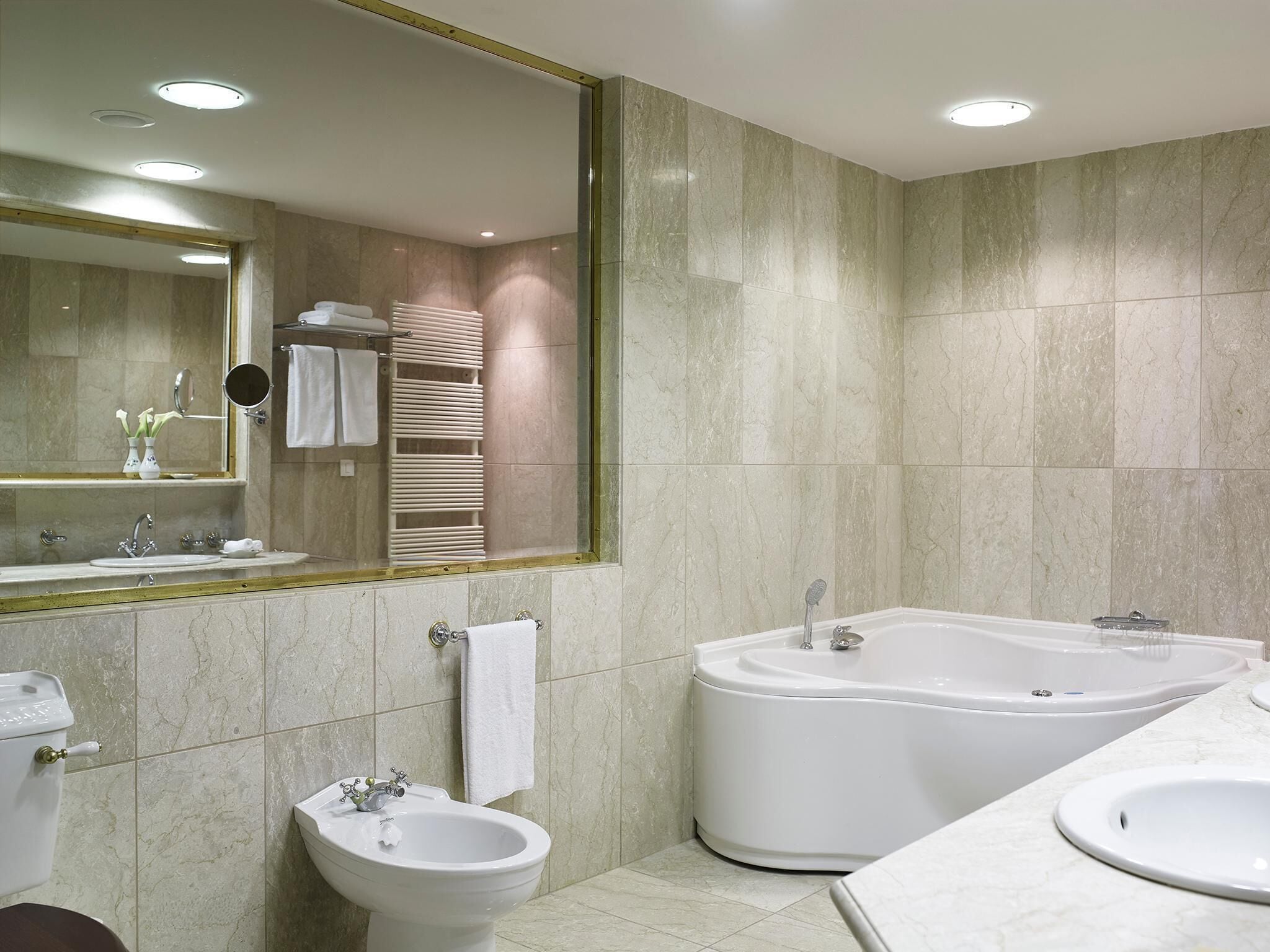 A modern bathroom with a large mirror, a bidet, a bathtub, and a sink.