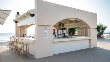A beach bar with a white exterior, bar stools, and a view of the ocean.