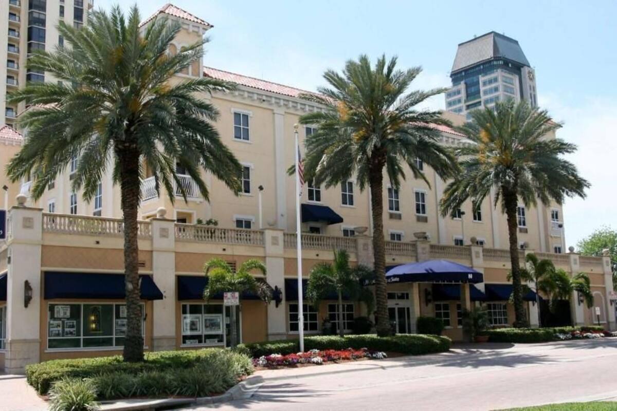 Un hotel con un letrero que dice 'Hampton Inn & Suites', palmeras y un cielo despejado.