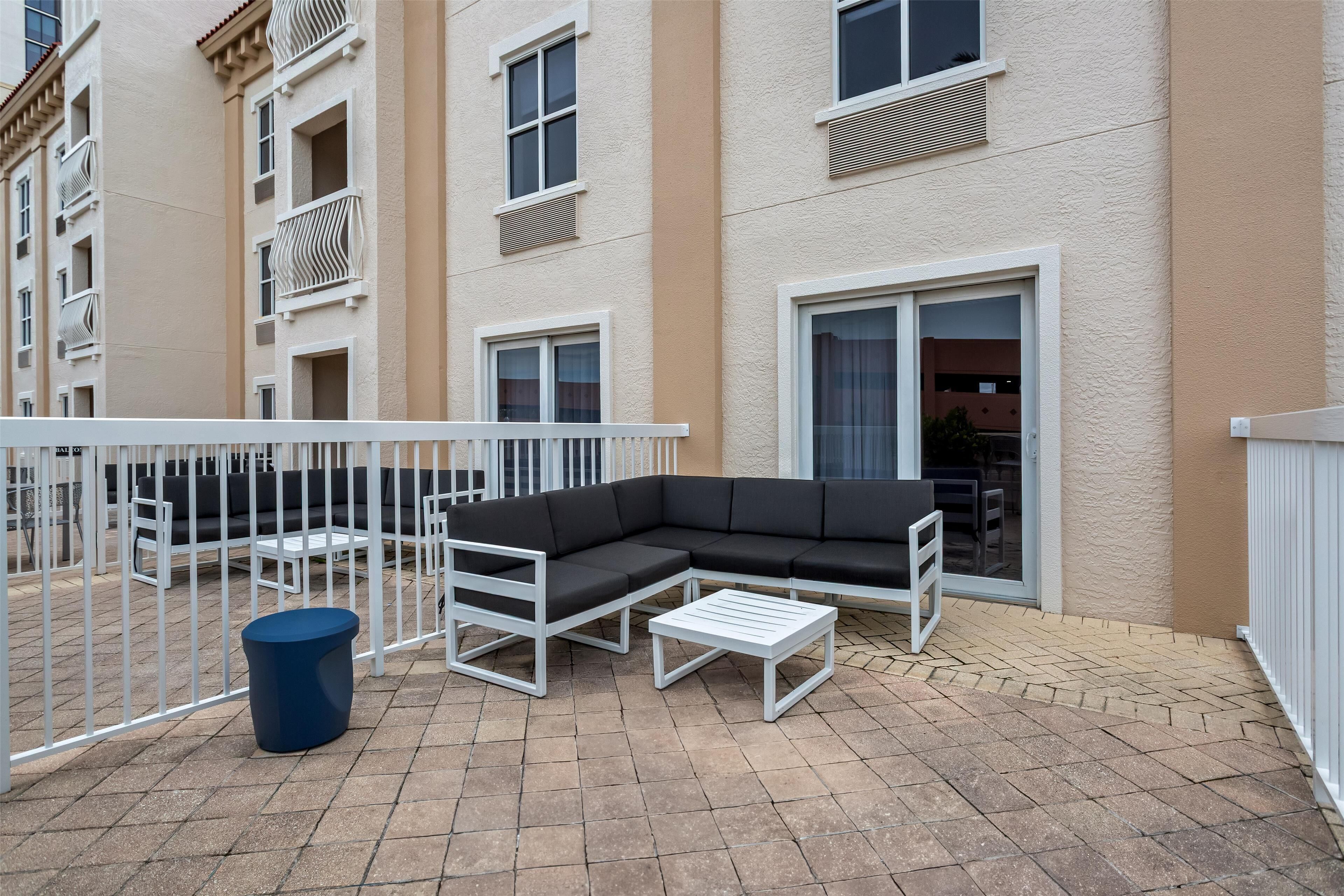 A modern outdoor patio with a sectional sofa, a small table, and a trash bin.