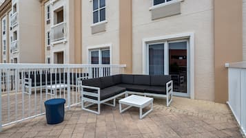 A modern outdoor patio with a sectional sofa, a small table, and a trash bin.