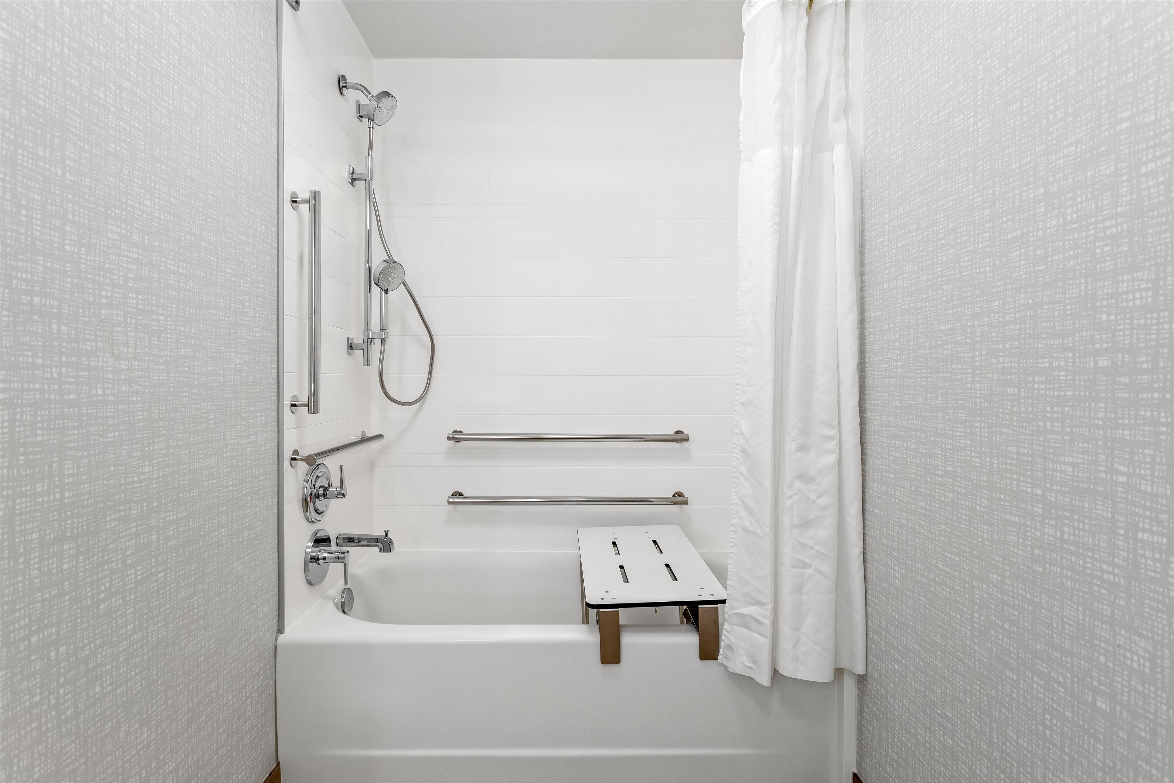 A white bathroom with a bathtub, a shower, and a small wooden stool.