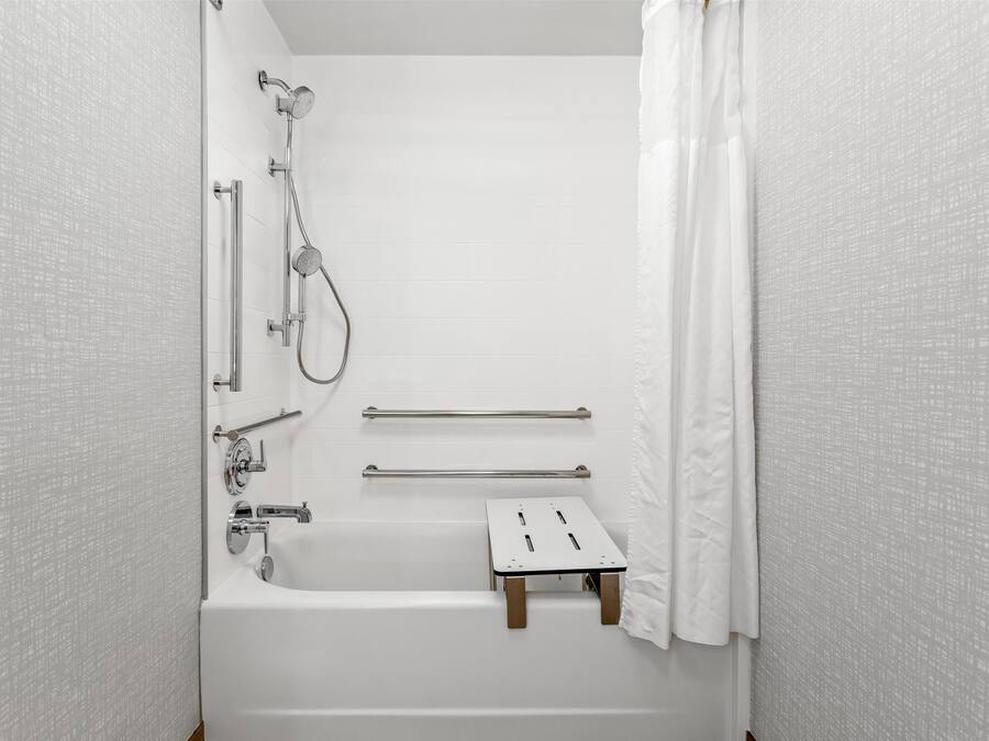 A white bathroom with a bathtub, a shower, and a small wooden stool.