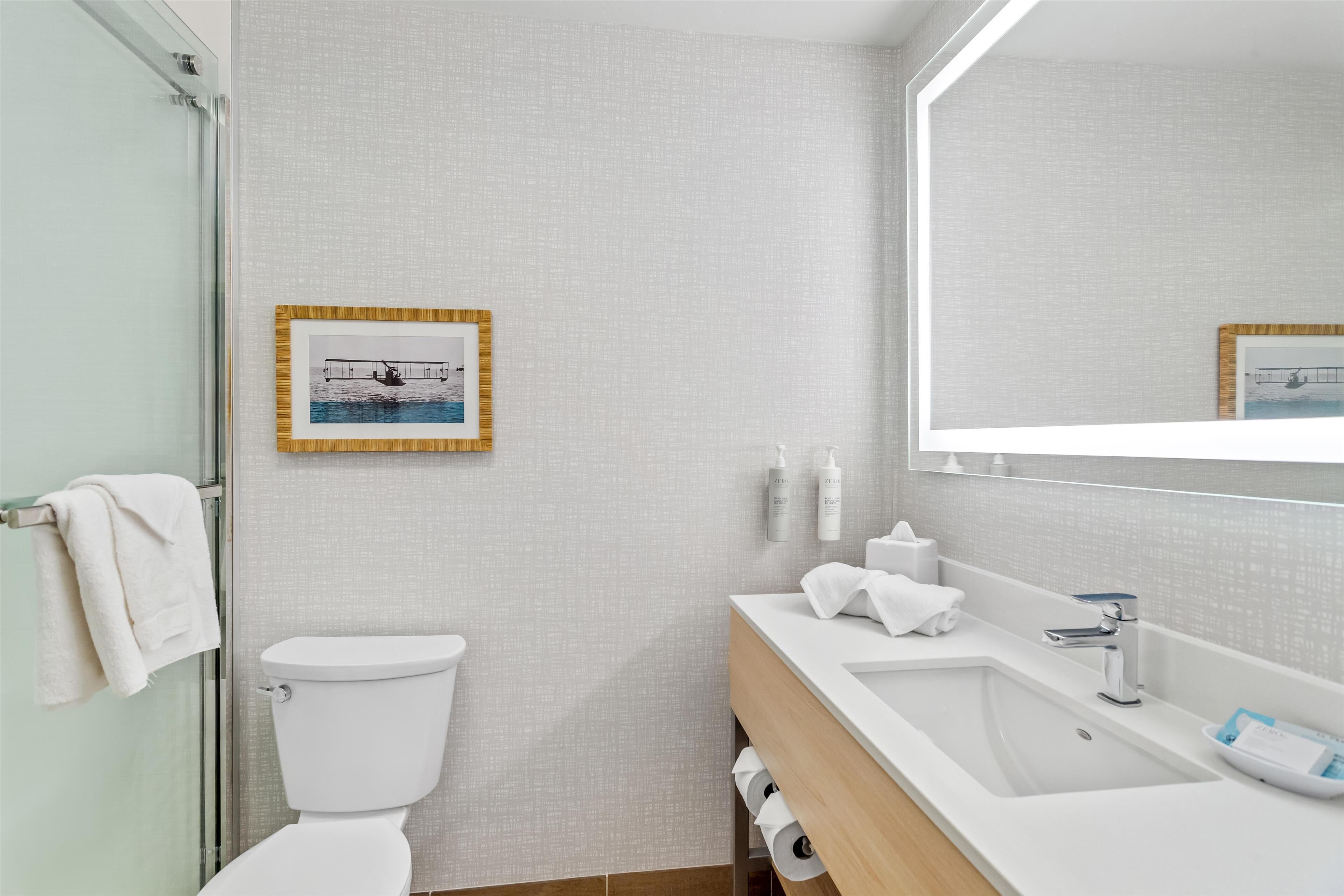 A modern bathroom with a glass shower enclosure, a white toilet, a wooden vanity with a sink, and a large mirror.