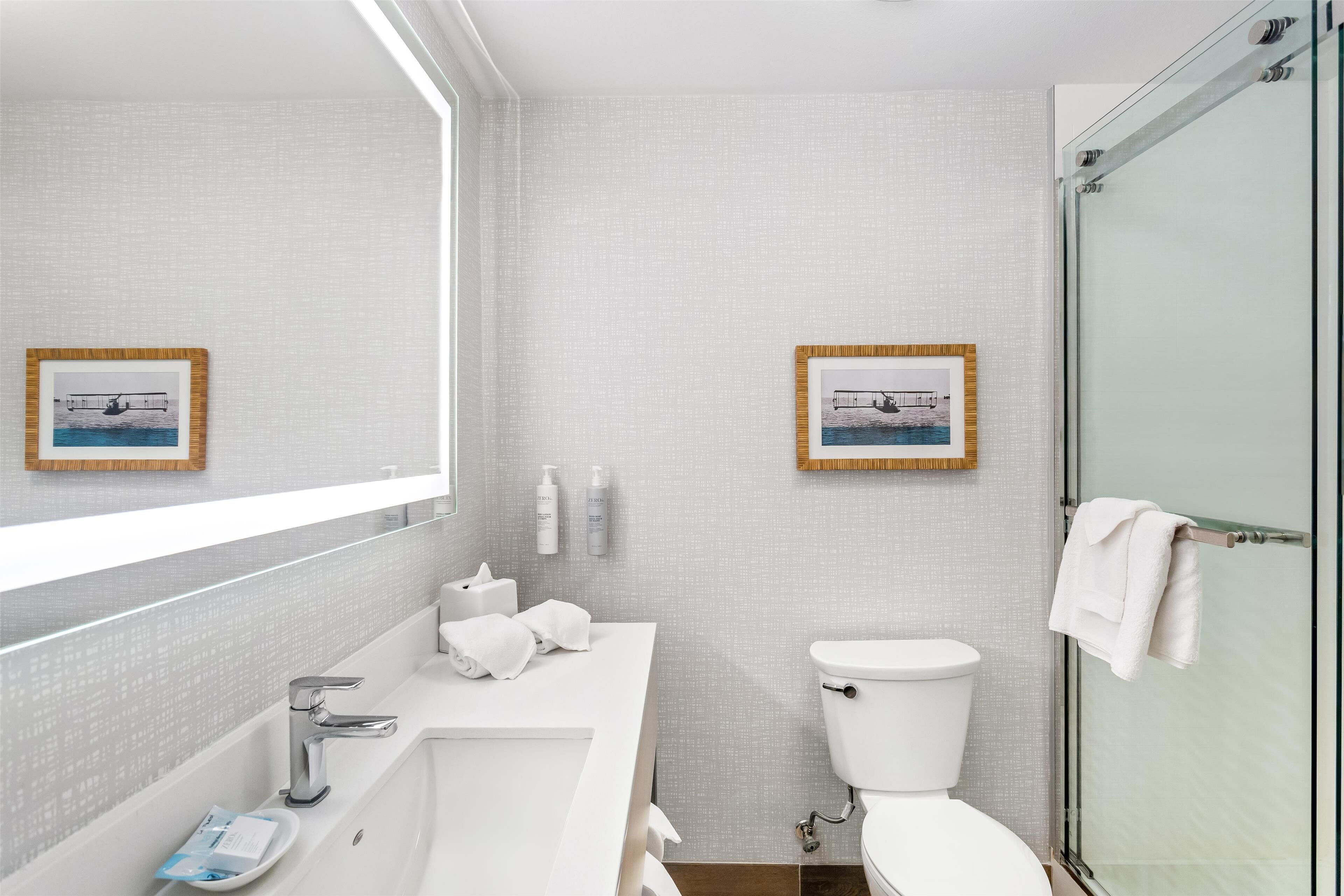 Un baño moderno con un espejo grande, un lavabo blanco, un inodoro y una cabina de ducha con paredes de vidrio.