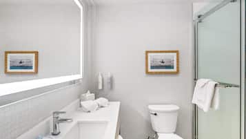 Un baño moderno con un espejo grande, un lavabo blanco, un inodoro y una cabina de ducha con paredes de vidrio.