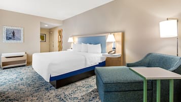 A hotel room with a large bed, a desk, a chair, and a lamp.