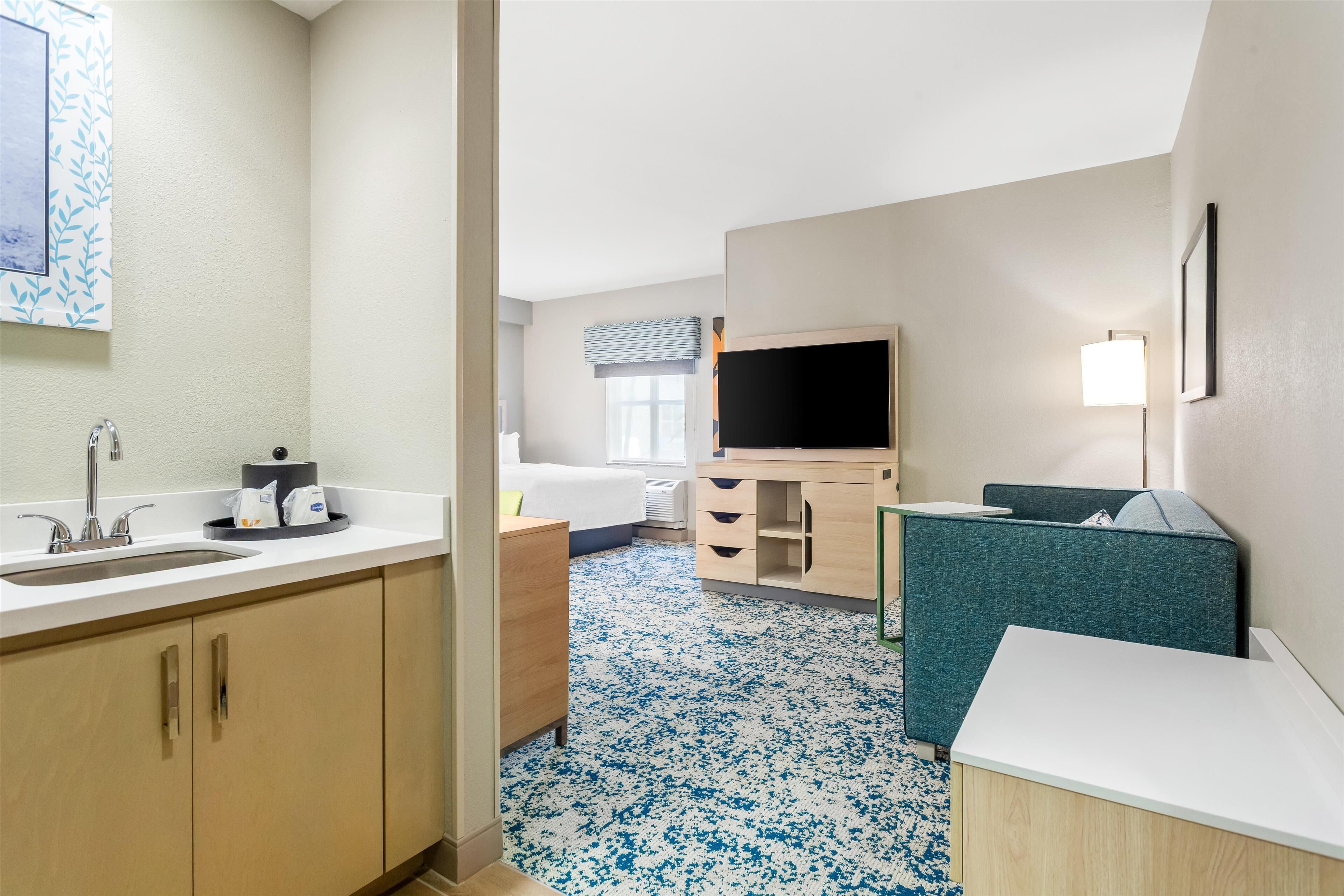 A hotel room with a sink, a bed, a TV, a desk, and a chair.