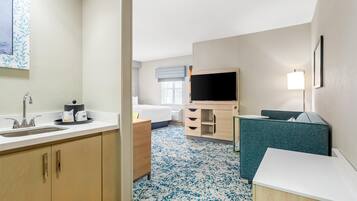 A hotel room with a sink, a bed, a TV, a desk, and a chair.
