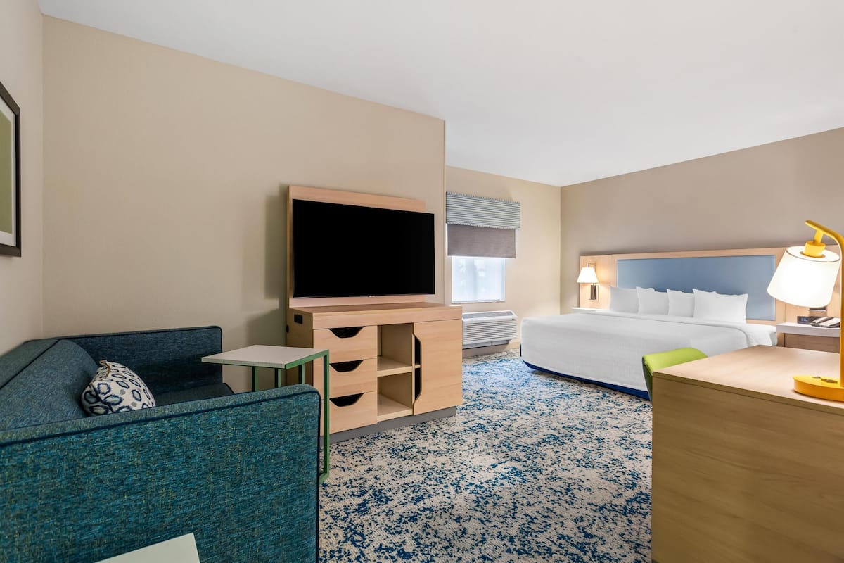 Habitación de hotel con cama, escritorio, televisor, silla y una mesita.