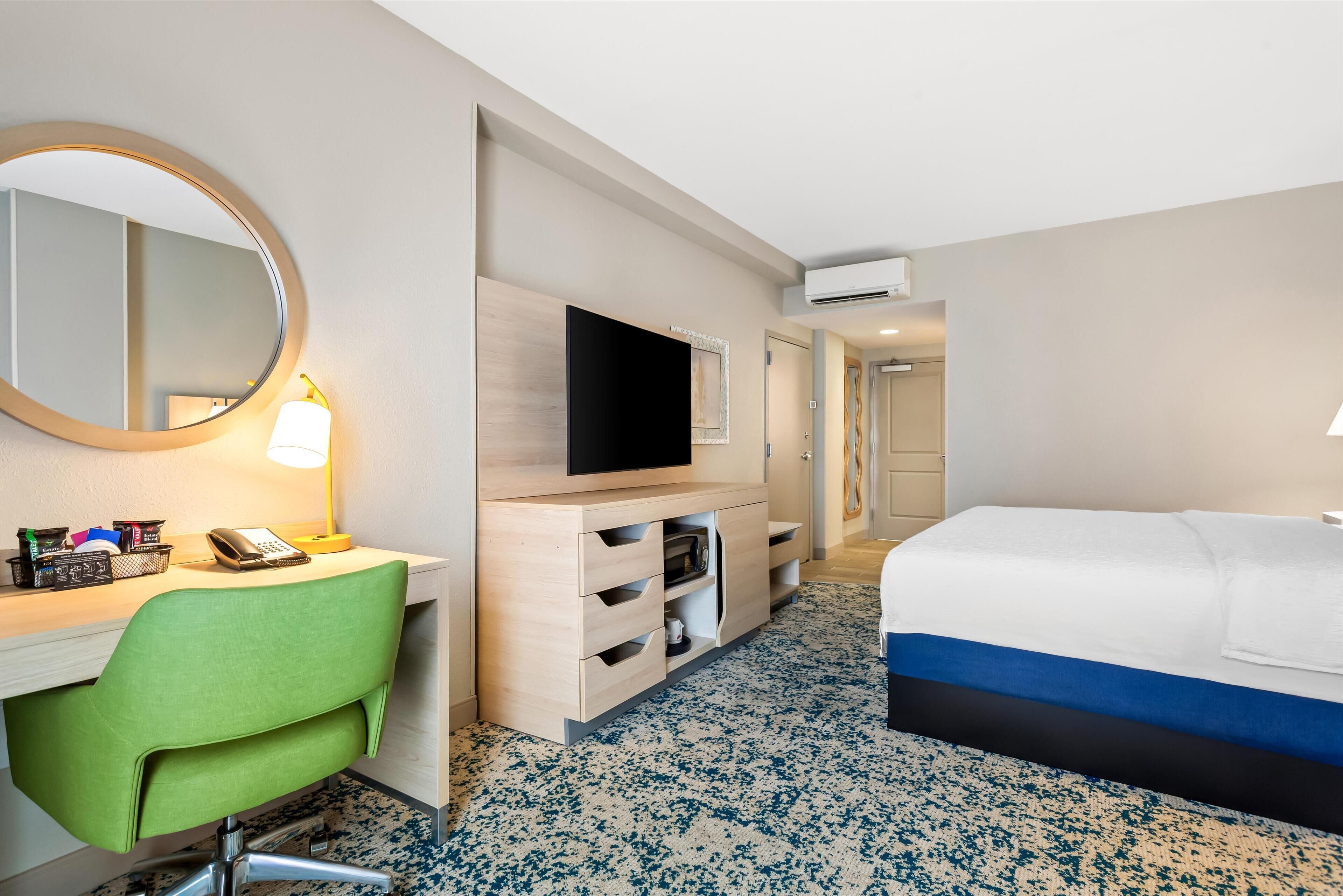 A hotel room with a bed, a desk with a chair, a television, and a mirror.