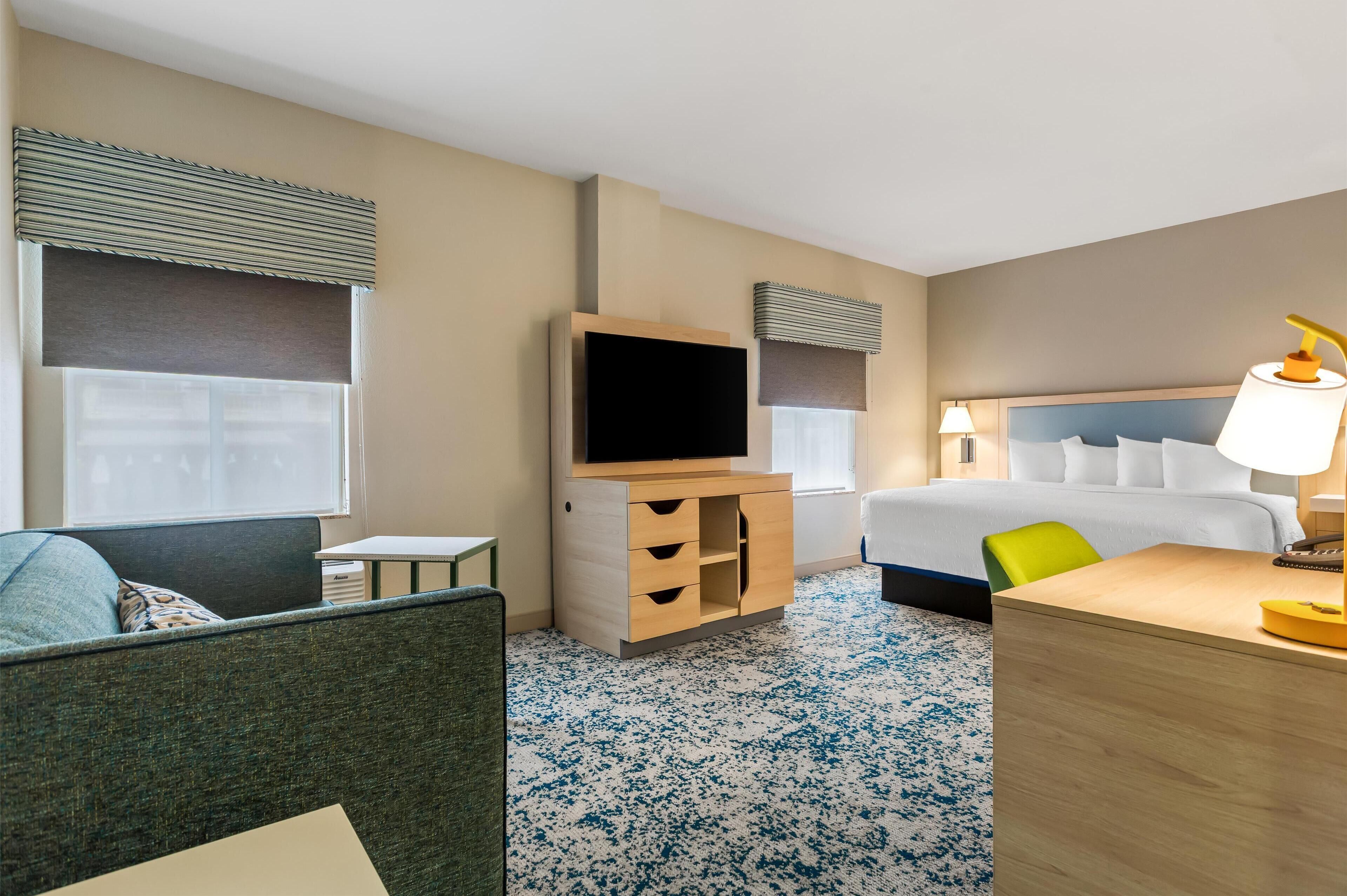 A hotel room with a bed, a desk, a television, a chair, and a sofa.