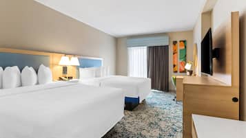 A hotel room with two beds, a desk, a TV, and a painting on the wall.