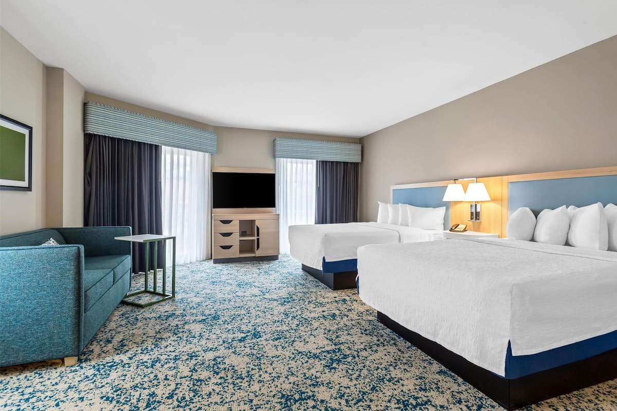 Habitación de hotel con una cama grande, dos camas más pequeñas, un sofá, un televisor, un escritorio y una lámpara.