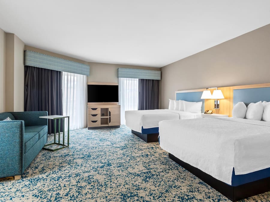 Habitación de hotel con una cama grande, dos camas más pequeñas, un sofá, un televisor, un escritorio y una lámpara.