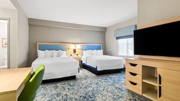 Habitació d'hotel amb dos llits, una taula de treball, una cadira, un televisor i una finestra.
