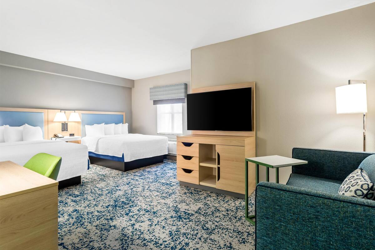 Una habitación de hotel con cama, escritorio, silla, televisor y una mesita.