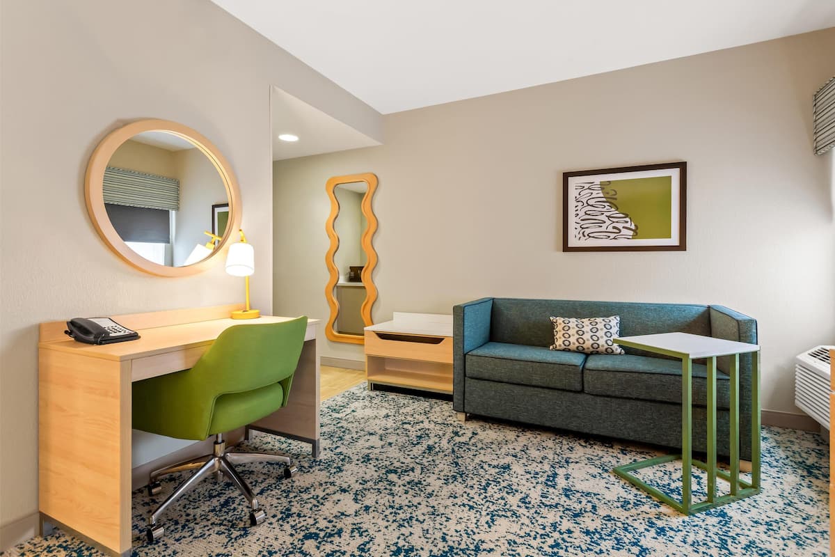 Una habitación de hotel con escritorio, una silla verde, un sofá azul y una pequeña mesa.