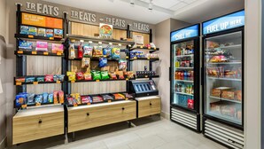 Un’area self-service con snack e bevande, assortimento di prodotti confezionati, cassa e distributori automatici refrigerati.
