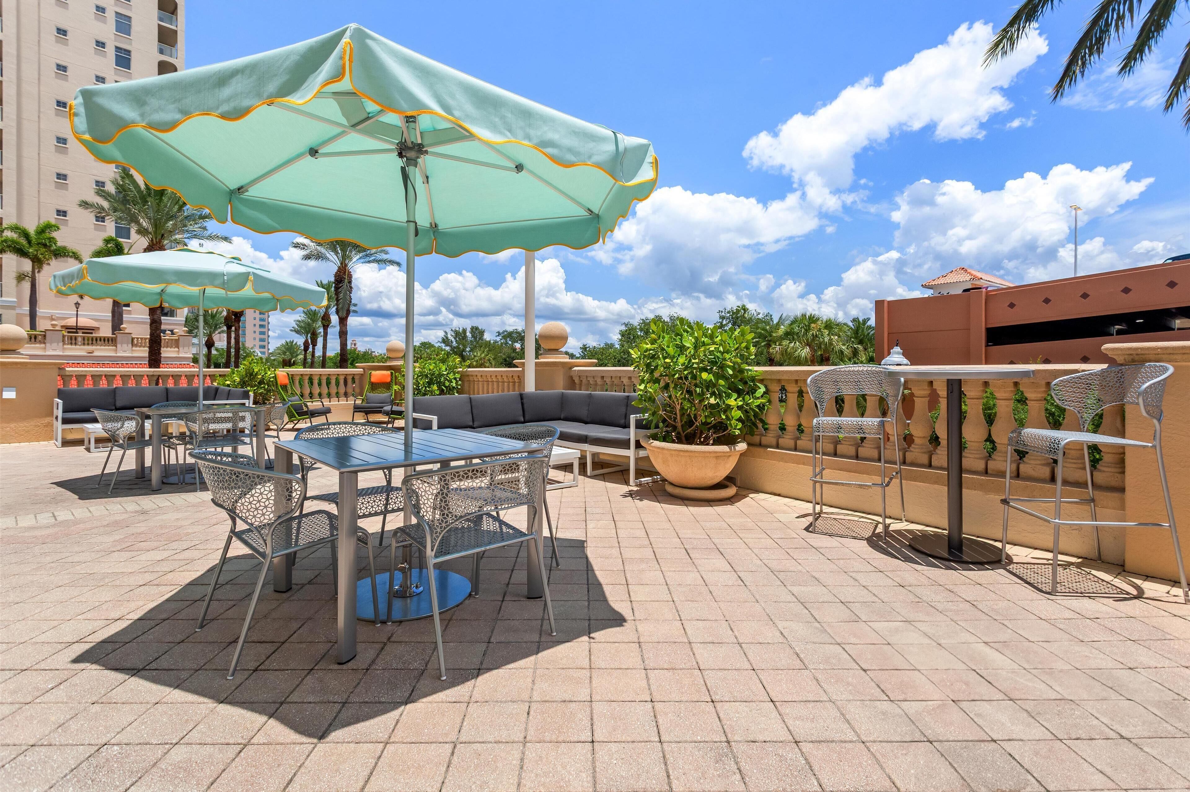 A rooftop patio with outdoor seating, including tables and chairs, and two large umbrellas providing shade.