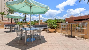 A rooftop patio with outdoor seating, including tables and chairs, and two large umbrellas providing shade.
