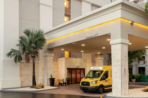 A hotel entrance with a clearway sign, a palm tree, and a yellow van.